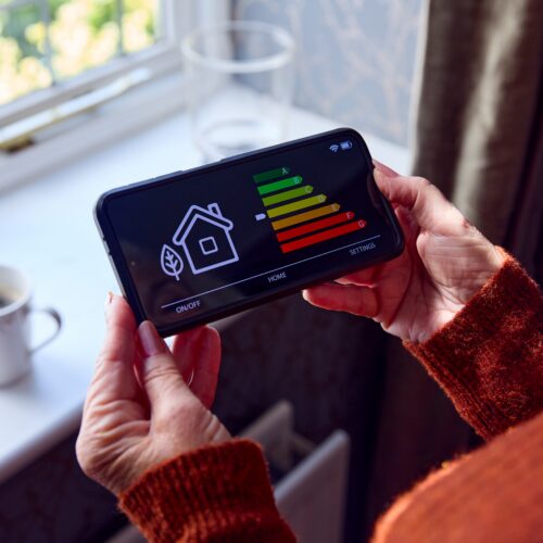 Senior person holding their smartmeter with a cup of tea to keep warm