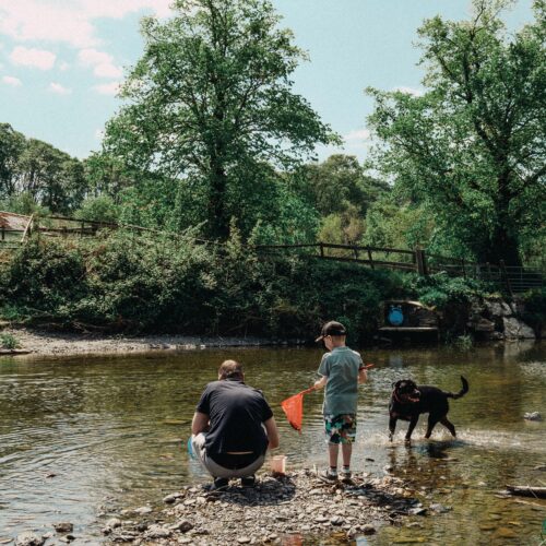 A father and son enjoying a fishing day by a river with their dog