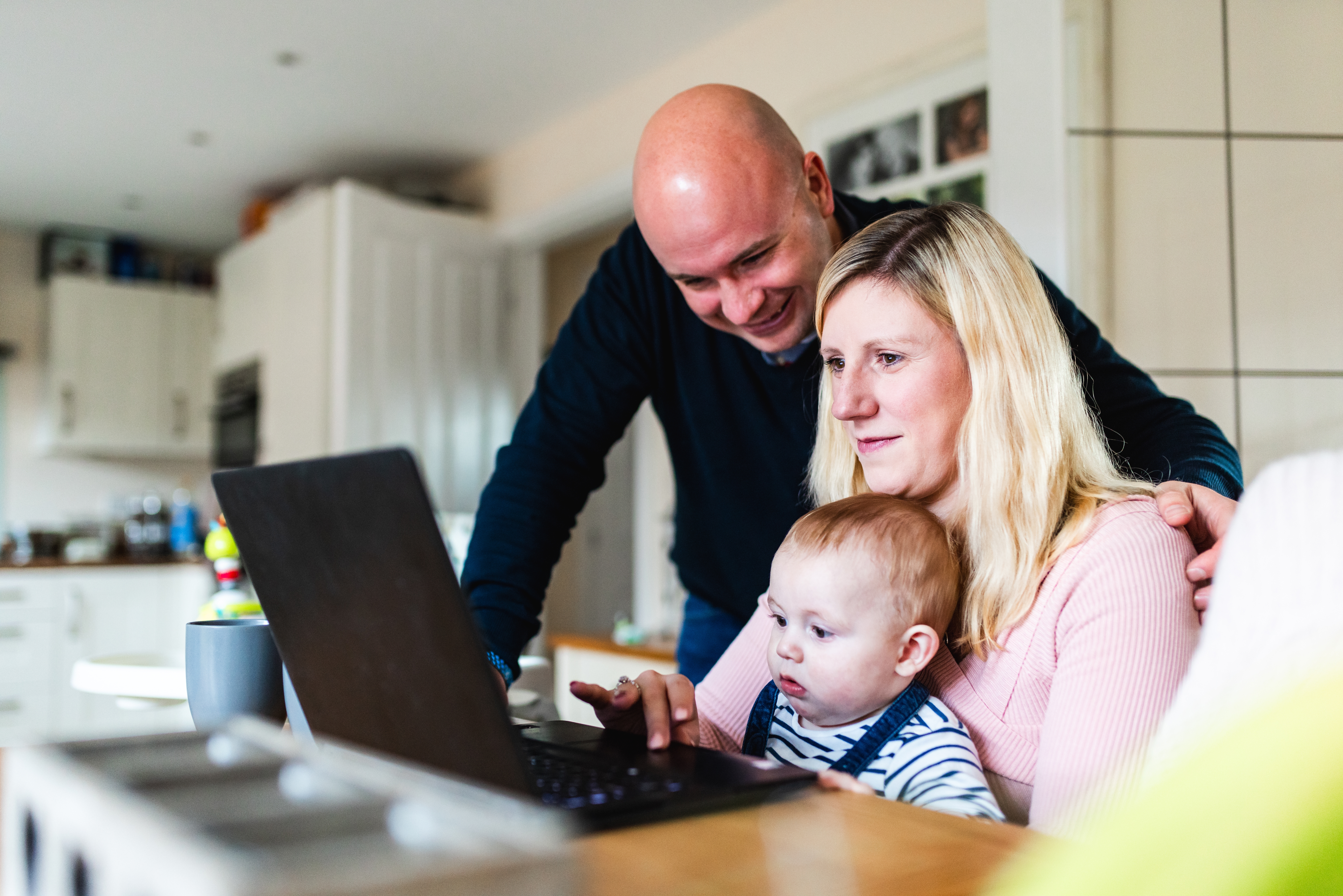A family of three - including a small child at the kitchen table, sat around a laptop together.