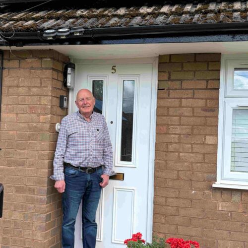 A man stood outside a bungalow with solar panels on the roof.