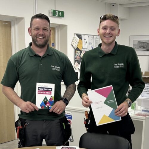 Two Housing Plus Group colleagues smiling and holding apprentice role promotional materials.