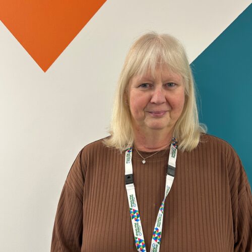 Our Money Matters Outreach Coordinator, Sharon Sinclair stood in front of a colourful branded wall at our head office.
