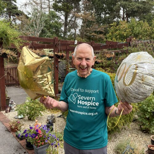 94-year-old man stood outside with celebratory balloons